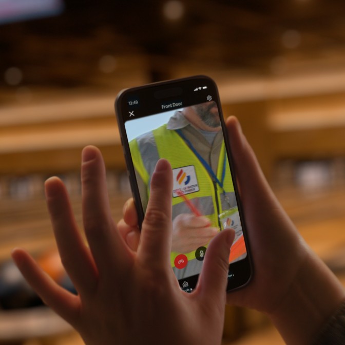 Close-up of someone holding a smartphone displaying footage of a delivery driver walking up a pathway