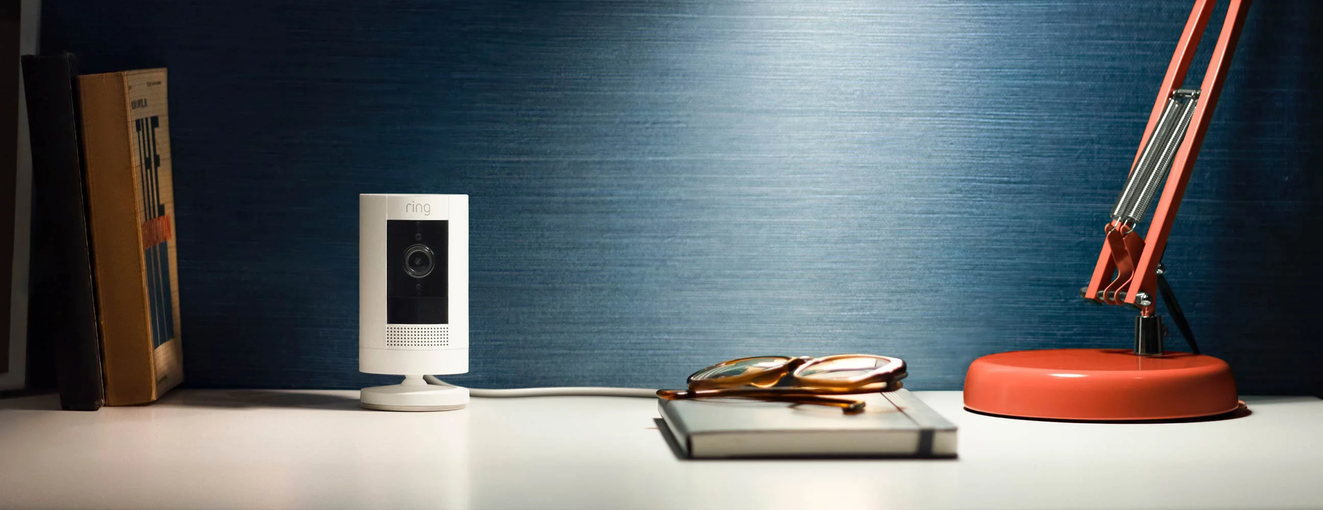 Cámara Ring Security Cam Plug-In blanca montada en pared de madera con cable de alimentación en la parte inferior.