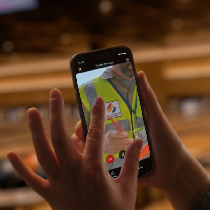 Primer plano de una persona con un smartphone en el que se muestra a un repartidor caminando por un camino