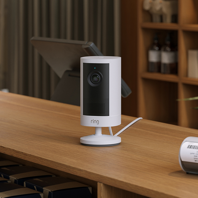 Ring Outdoor Camera 4K Plus, placed on a wooden desk in a bright home office.