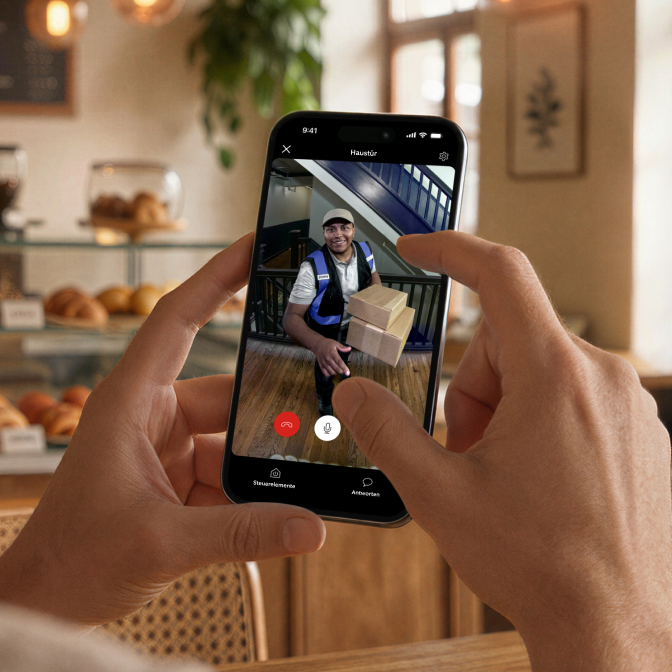 Eine Person im Restaurant verfolgt über das Live-Video des Video-Türspions 2K auf ihrem Smartphone, wie ein Paketbote gerade ein Paket an der Tür zustellt.