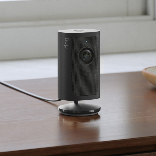 Ring Indoor Camera 4K on a circular base, placed on a wooden desk in a home office setting with power cable attached.