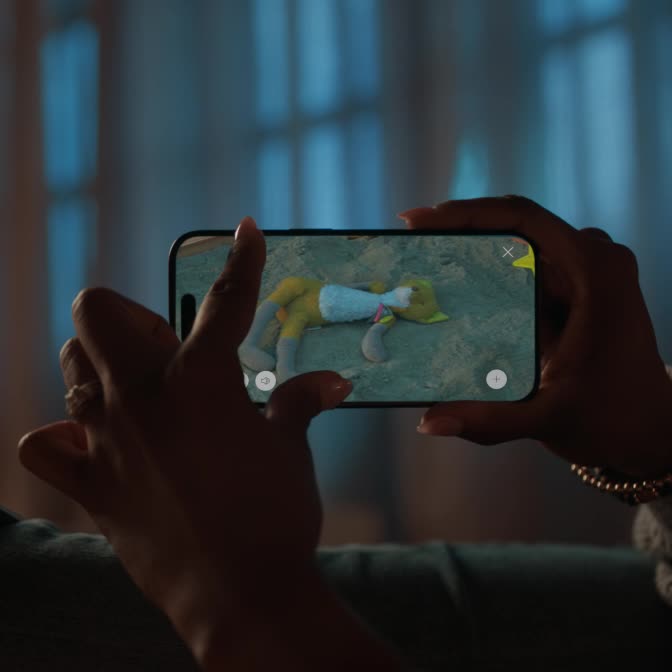 Hands hold phone, fingers zoom into footage showing lost toy fox in sand-box, followed by relieved mother and daughter finding it