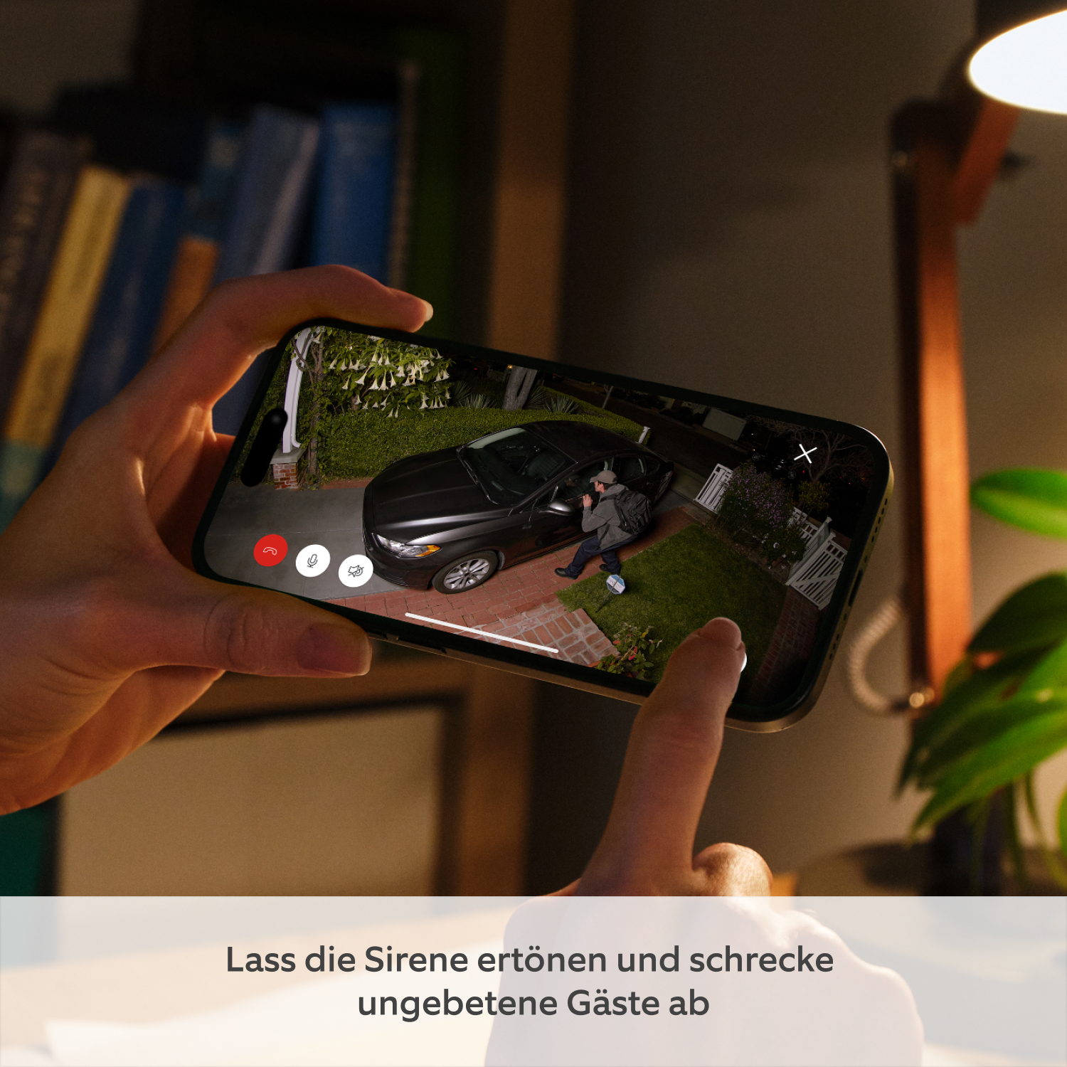 Spotlight Kamera Pro (neueste Generation) mit Netzteil (for Spotlight Cam Pro Plug-In (2. Gen.)) - Hände halten Smartphone mit Ring-App-Aufnahme einer Person, die nachts ein Auto inspiziert, beleuchtet von Spotlight Cam Pro. Finger tippt Sirenen-Button