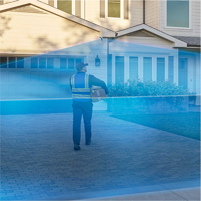 A delivery driver walks into a driveway covered in a blue laser graphic extending out from a Ring Outdoor Camera Pro mounted to the house.