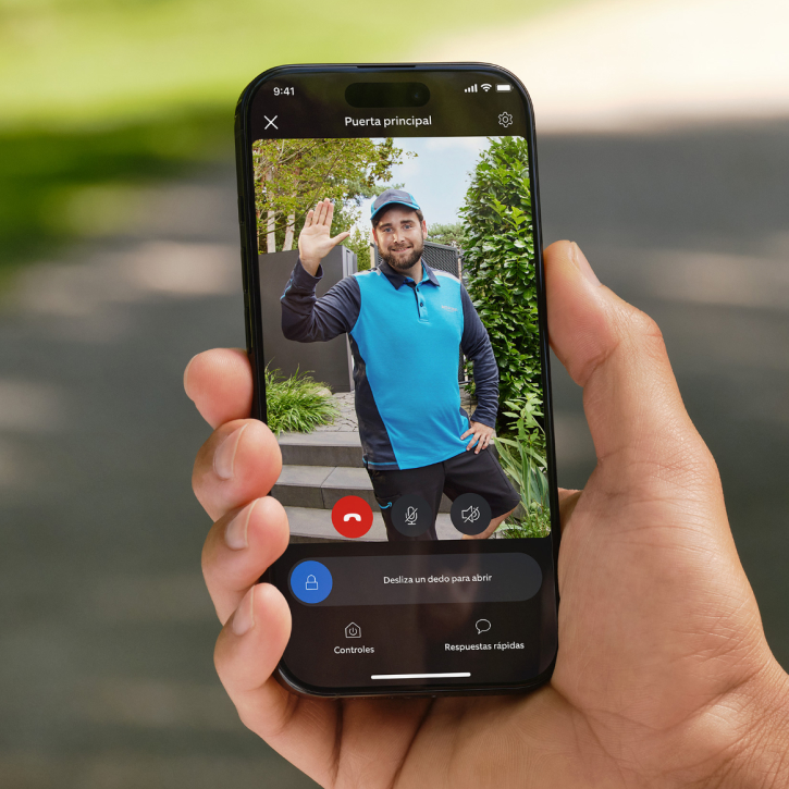 Close-up of someone holding a smartphone displaying footage of a technician in front of a gate.