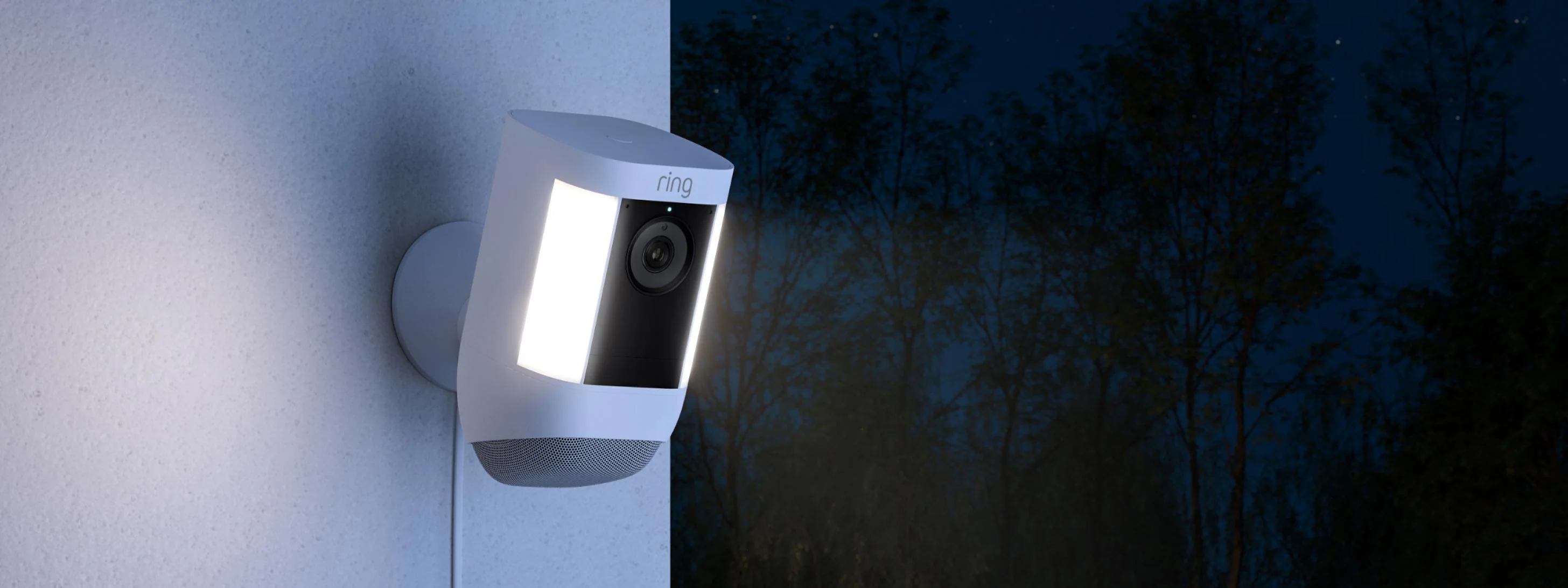Ring Spotlight Cam Pro gemonteerd op muur in het donker met zijlampen aan, maakt video-opnames bij weinig licht.