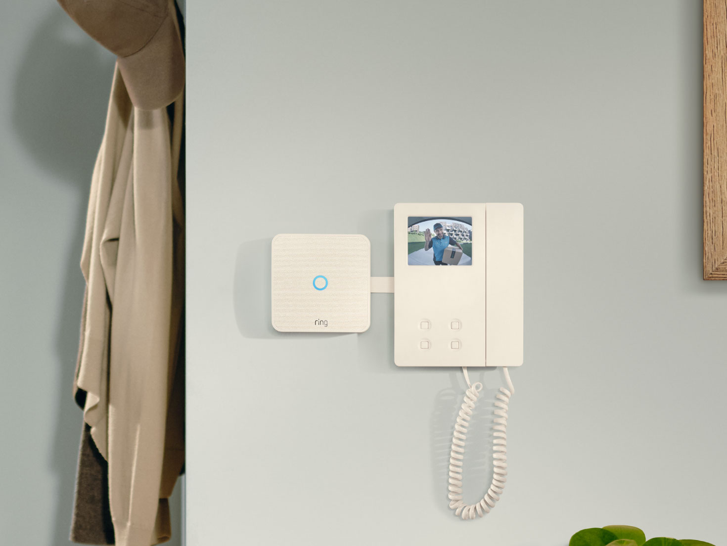 Ring Intercom-Gerät an der Wand neben einem traditionellen Telefonhörer montiert, mit grüner Pflanze im Vordergrund.