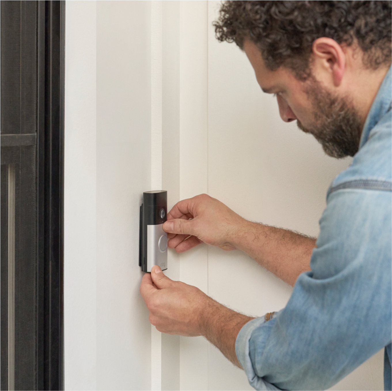 Image shows a man securing a Wired Video Doorbell Plus onto its mounting bracket beside the front door
