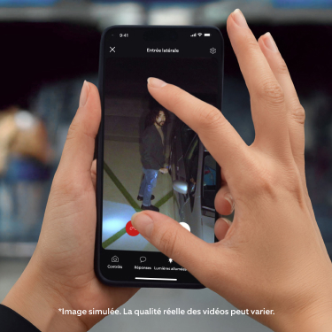 Mains tenant un smartphone affichant l'application Ring avec le flux vidéo en direct de la Floodlight Cam (2e gén.), montrant une personne suspecte à côté d'une voiture. Un doigt et un pouce pincent l'écran du smartphone pour zoomer.
