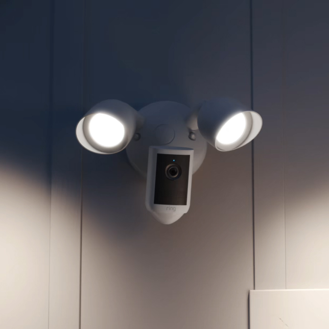 Une Floodlight Cam (2e gén.) blanche installée sur le pignon avant blanc d'une maison.