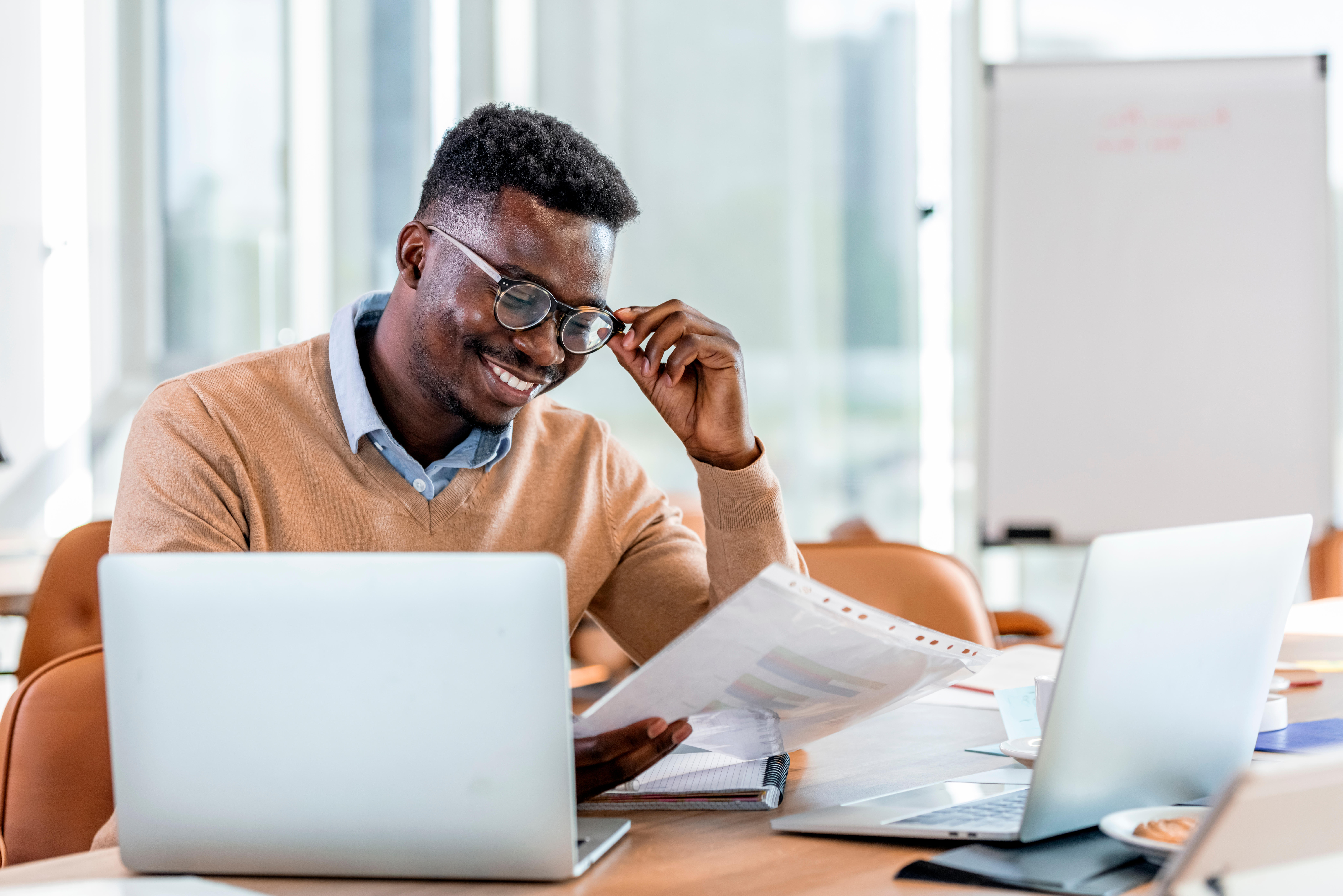 Man with computer and files, looking at piece of paper.