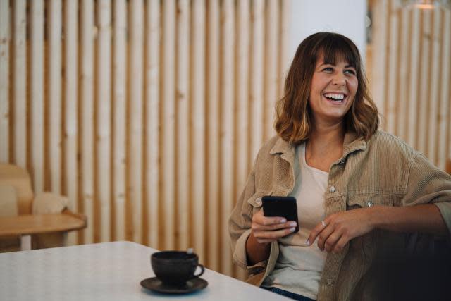 Woman smiling while holding phone, drinking coffee