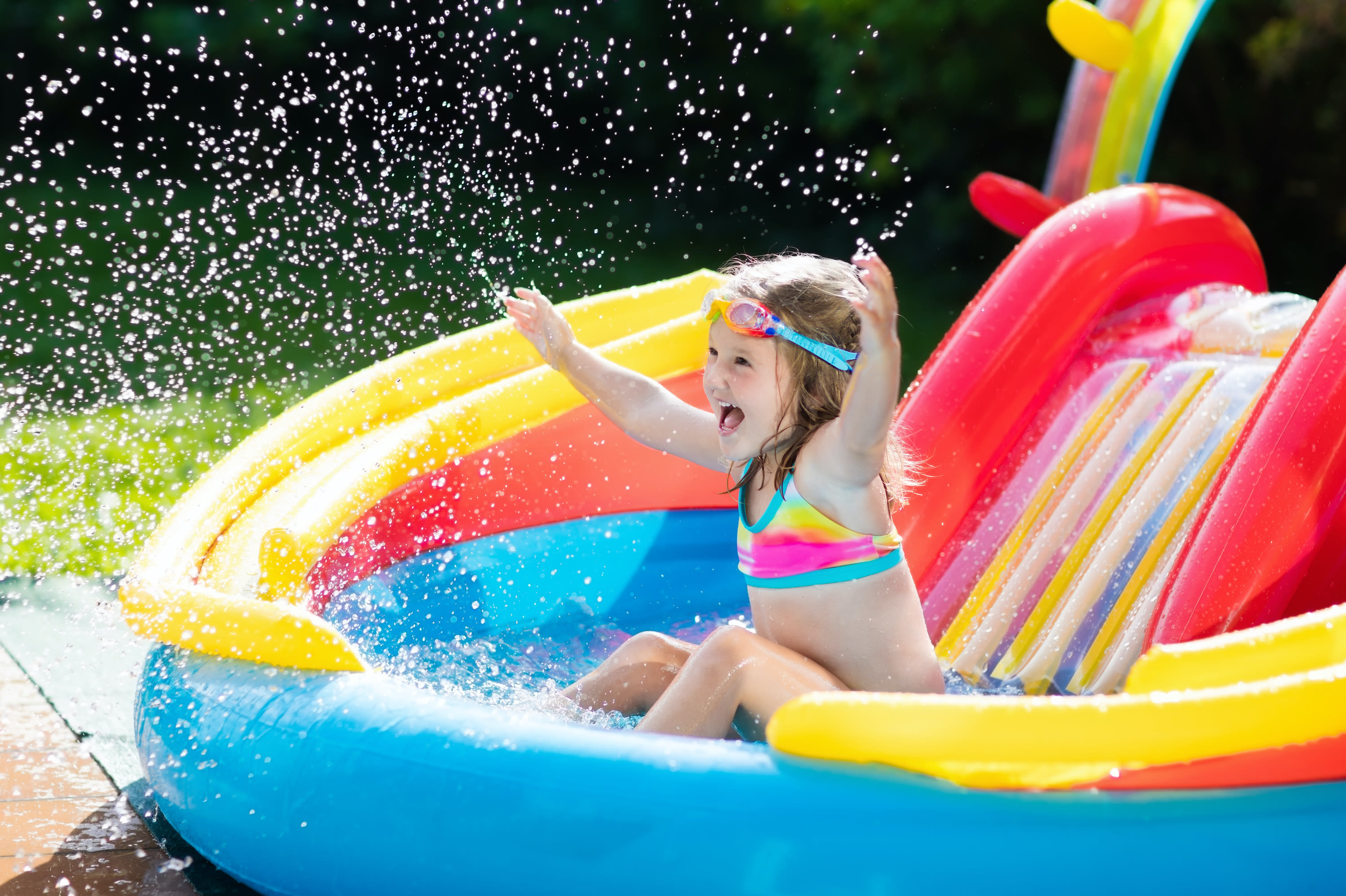 Meisje speelt met water in opblaaszwembad met glijbaan. Foto: Adobe Stock / famveldman