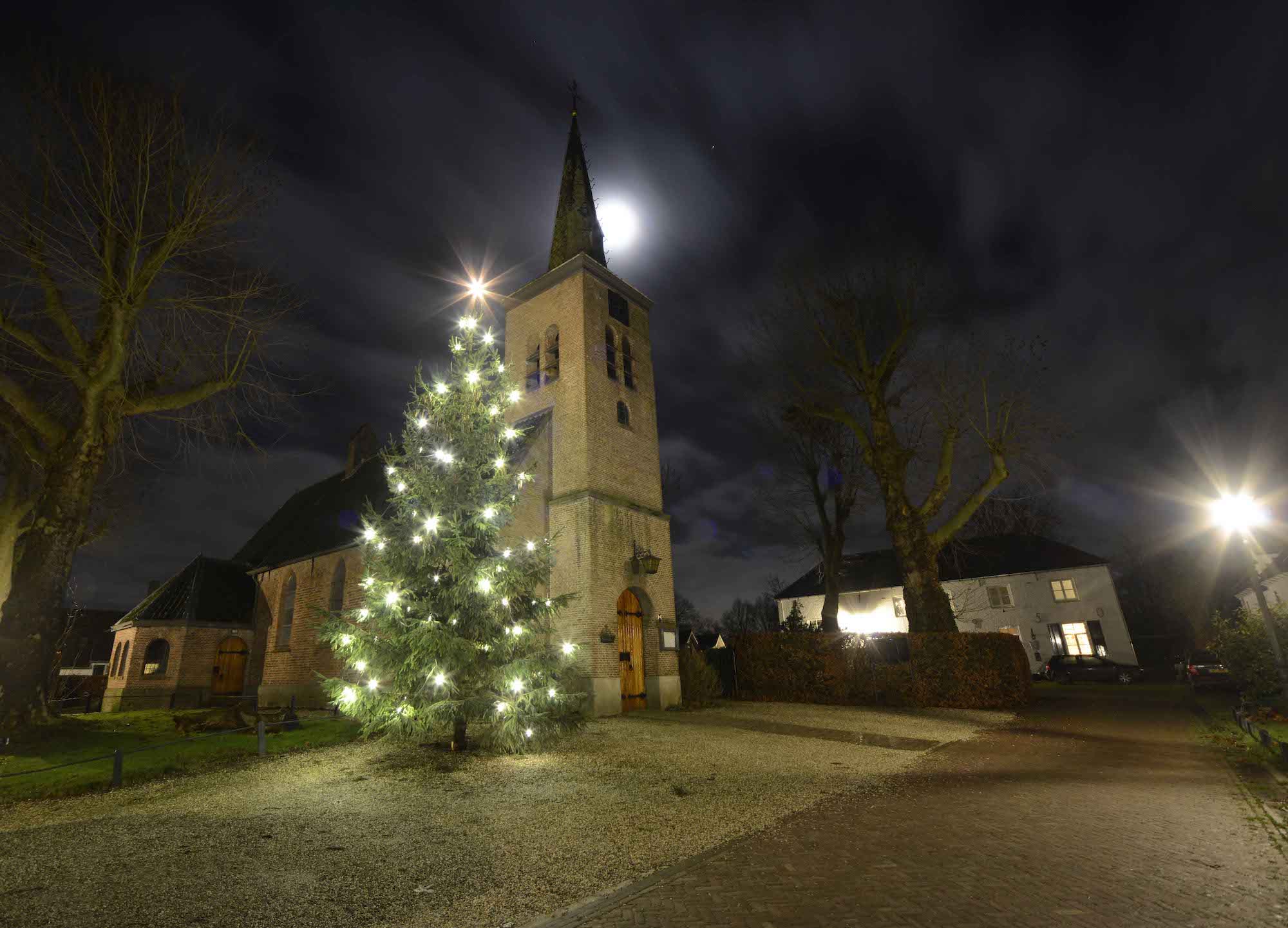 Donkere dagen voor kerst kerstboom bij kerk met maanlicht en kale bomen. Foto: Ton Timmer