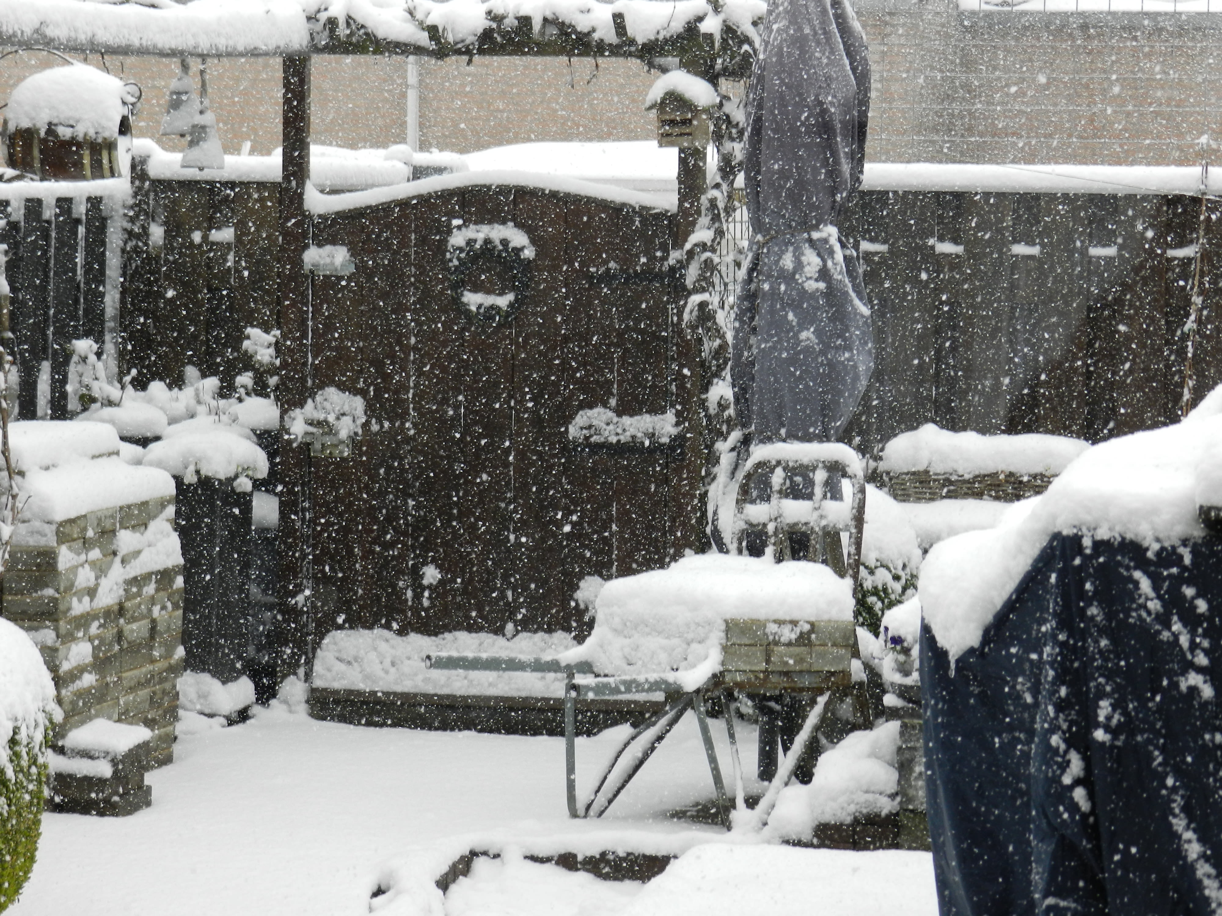 Dik pak sneeuw en sneeuwval in tuin met tuinmeubelen