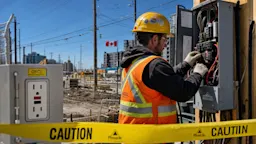 Construction worker in orange PPE working near an electrical panel on a Canadian construction site.