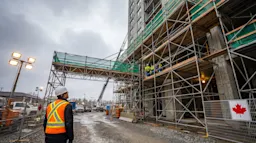 Site supervisor in high-visibility vest inspecting a large tubular steel scaffold system on a Canadian construction site.