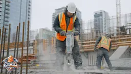 Construction worker wearing earmuffs and high-visibility vest operating a jackhammer on a Canadian construction site