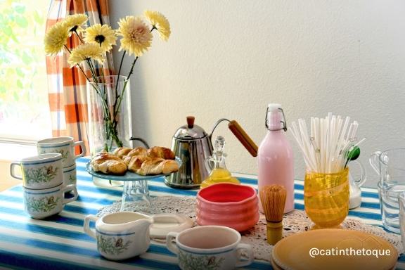 Instagram handle @aaricanichole. Brunch table packed with multicolored plates, mugs, and bowls.