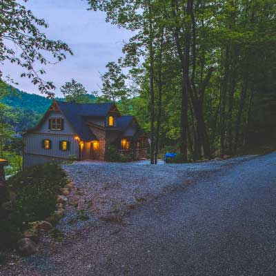 A gravel driveway leads to a lake house in the mountains of Western North Carolina at dusk.