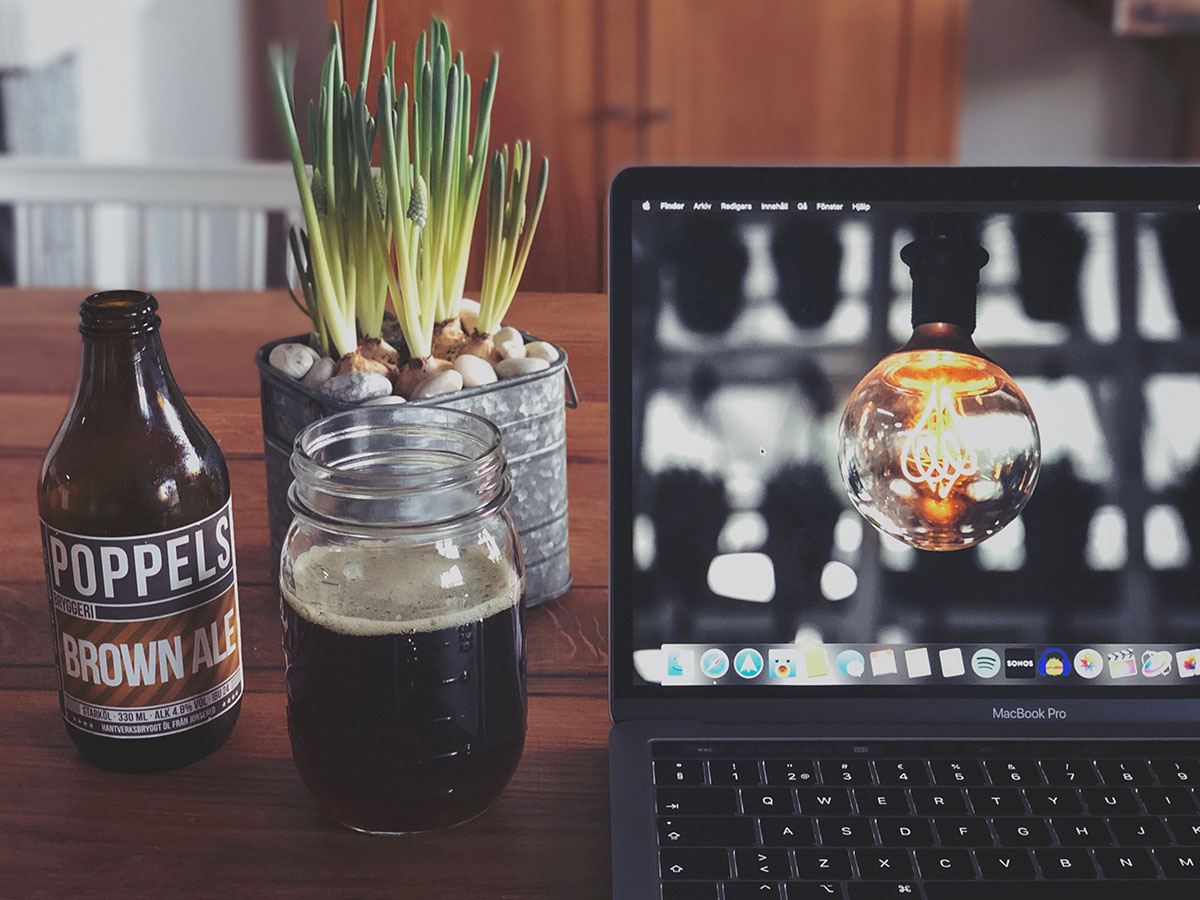 Desk with a laptop, beer bottle, cup, and a plant.