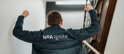 A man in a stairwell, wearing a jacket with the NoA Ignite logo.