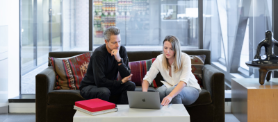 Two individuals are sitting on a sofa with a computer.