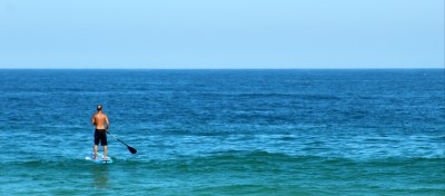 A man paddling on a board in an empty sea.