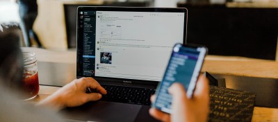 Hands working on a laptop and holding a phone.