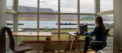 Woman working on the computer in the glass room with a view of the lake and the peaks.