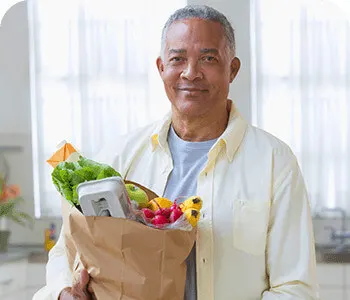 Um senhor idoso na cozinha com um saco de compras