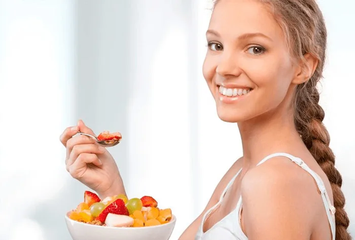 uma jovem sorridente comendo frutas frescas de uma tigela