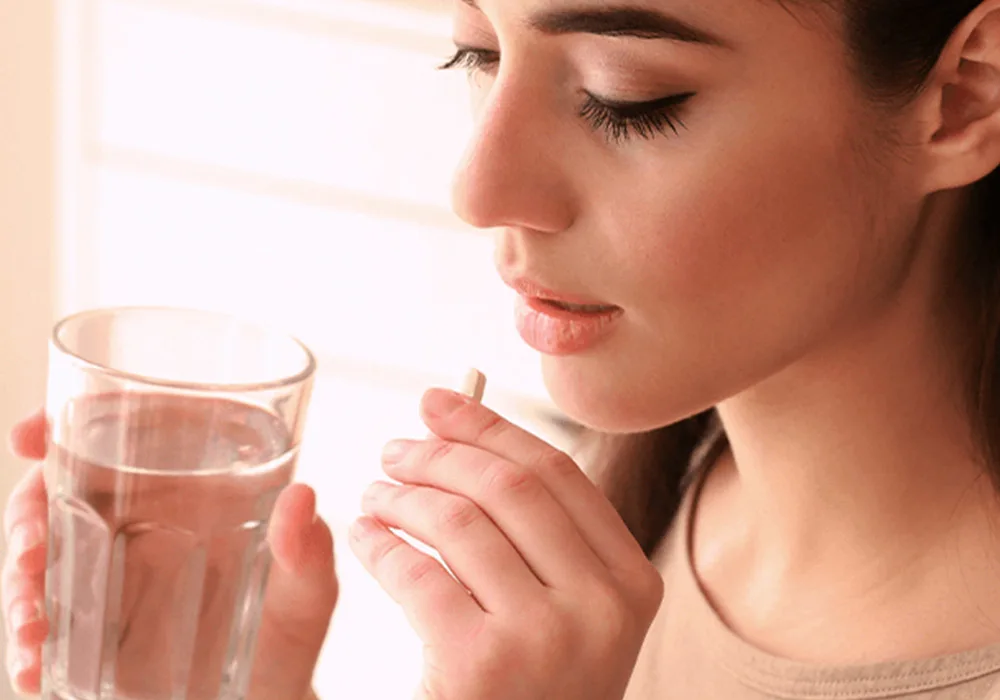 Mulheres segurando um copo d'água e tomando um comprimido de vitaminas no pré-natal