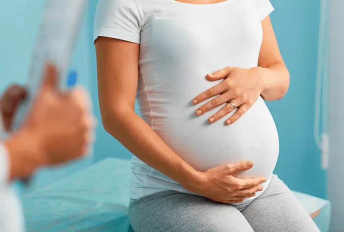 uma mulher grávida segurando a barriga com as duas mãos durante uma consulta médica
