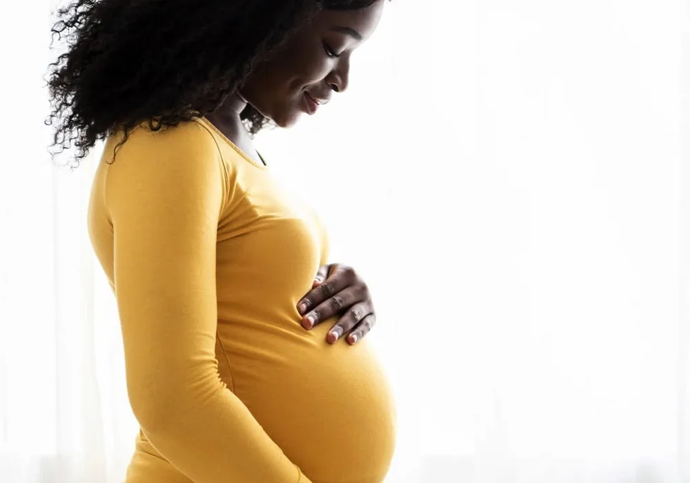 Mulher a tocar na barriga, com um teste de gravidez na mão