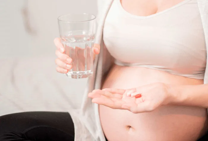 mulher grávida tomando comprimidos com água