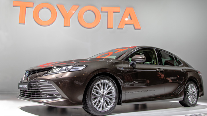 Berlina Toyota Camry Hybrid esposta sotto il grande logo Toyota.