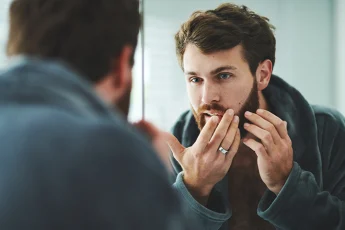 Mężczyzna w lustrze ogląda twarz z niedoskonałościami.