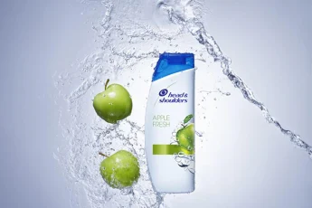 Dwa zielone jabłka i woda odbijają się od butelki  szamponu Head&Shoulders.