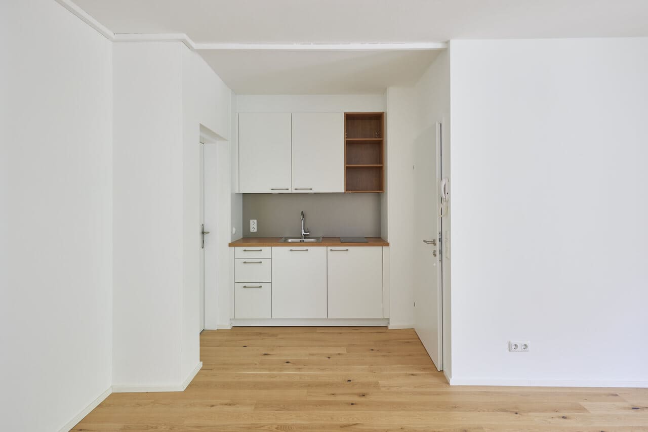 An empty kitchen with white cabinets and wooden floors