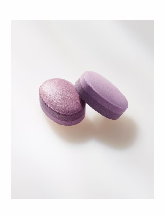 Two purple melatonin sleep aid tablets on a white background.