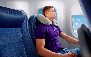A man sleeping comfortably in an airplane seat with an inflatable neck pillow.