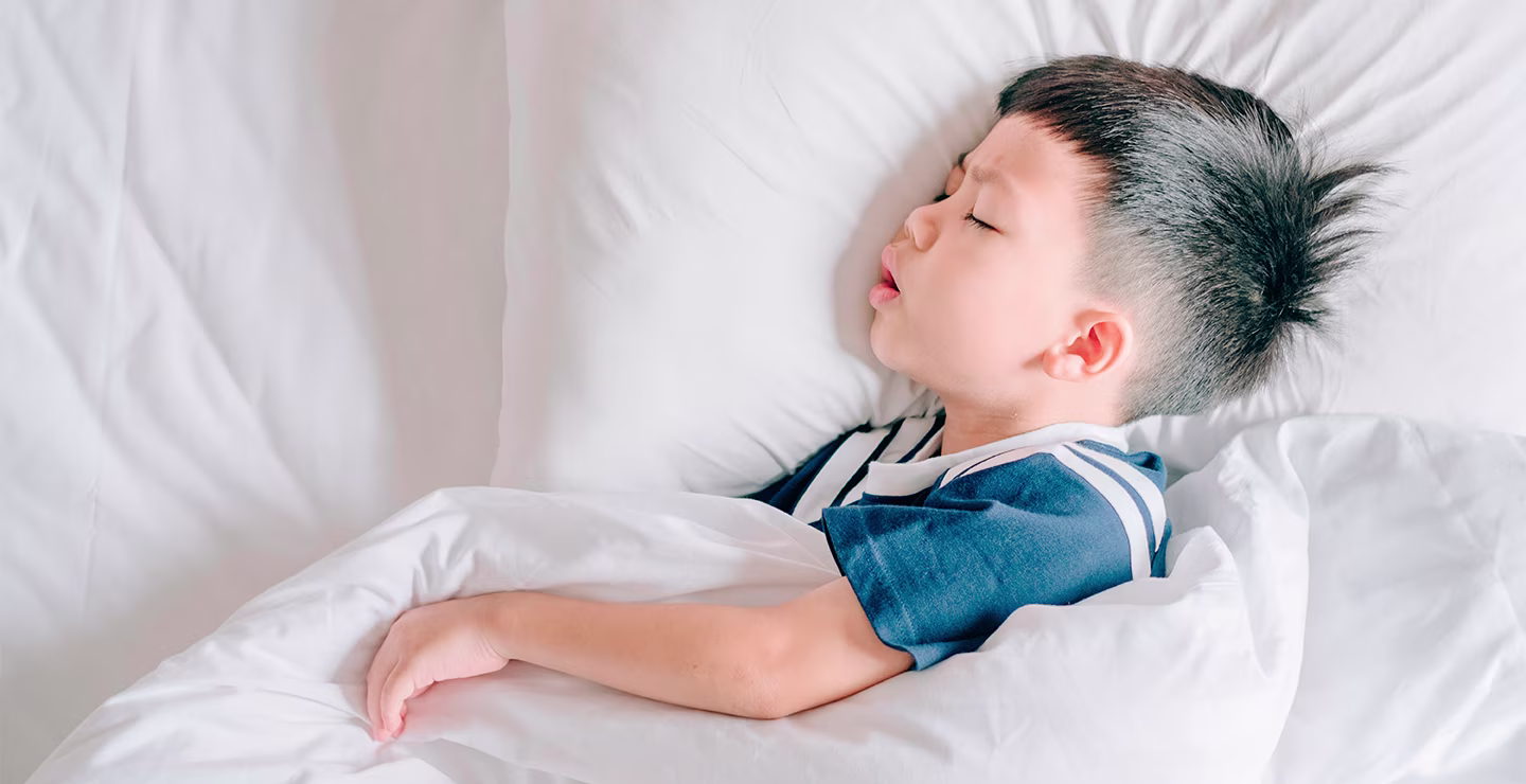 A young boy sleeping in a white bed.