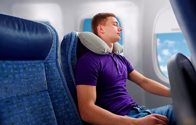 A man sleeping comfortably in an airplane seat with an inflatable neck pillow.