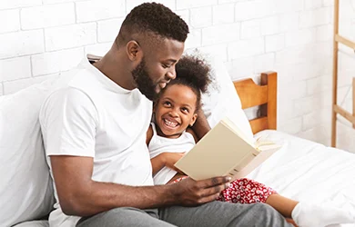 Help children fall asleep: dad reading a bedtime story to help his daughter to fall asleep. 