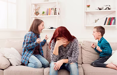 Women sitting on a couch with head in hand while two children yelling at each other.