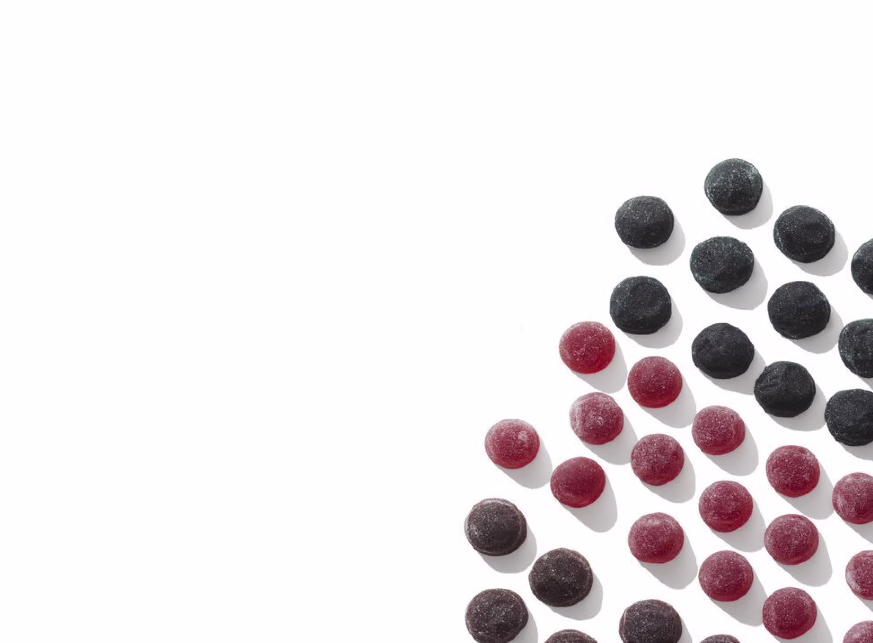 Multiple red and black berry-flavored melatonin gummies neatly arranged in diagonal rows on a clean white surface.