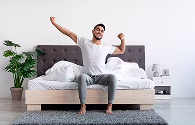 A man stretching after waking up from a good night's sleep, plants in the background.