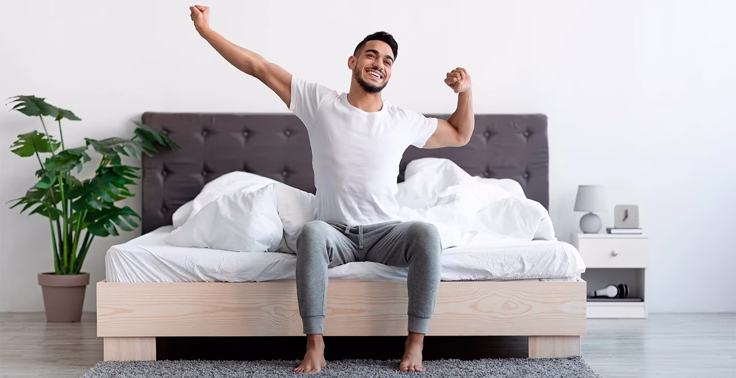 A man stretching after waking up from a good night's sleep, plants in the background.